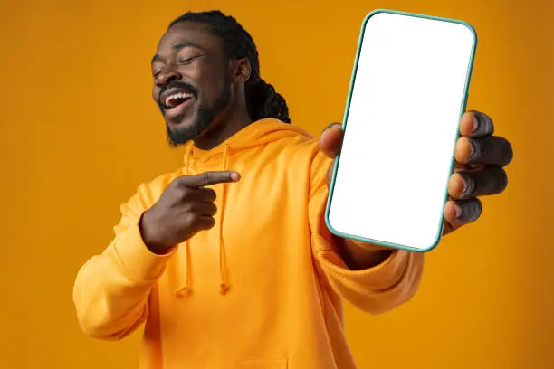 Smiling african man pointing at cellphone with blank screen with copy space against yellow background