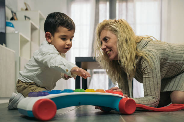 istock Frontal image of a little boy with special needs as he has a disability kneeling next to his smiling middle-aged blonde mother trying to play the musical colored keys. 1471626703