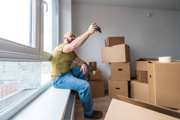 Adult man making selfie at the window sill in the room full of cardboard boxes