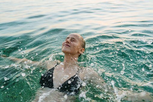 Photo of a smiling teenage girl, spending summer afternoon on the local beach: bathing, swimming and having fun