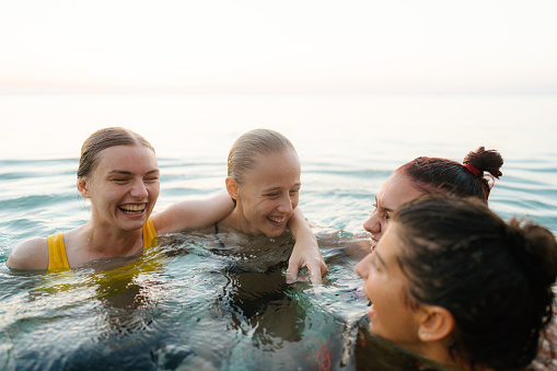 Photo of a smiling teenage girls, spending summer afternoon on the local beach: bathing, swimming and having fun