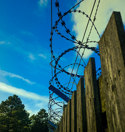 This razorwire is on top of a wooden fence,  with a blue sky background. Sending a strong signal of low tech security.