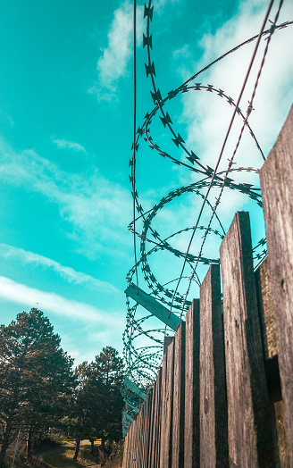 This razorwire is on top of a wooden fence,  with a blue sky background. Sending a strong signal of low tech security.