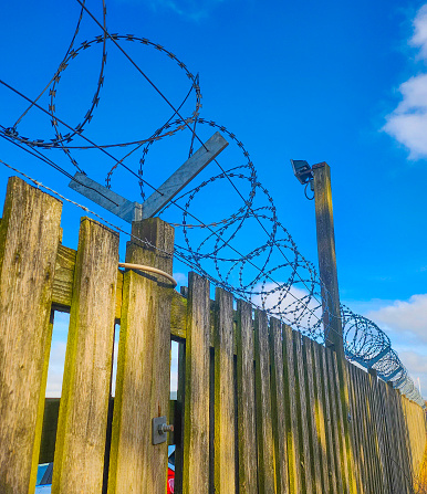 This razorwire is on top of a wooden fence , with a blue sky background. Sending a strong signal of low tech security.