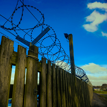 This razorwire is on top of a wooden fence , with a blue sky background. Sending a strong signal of low tech security.