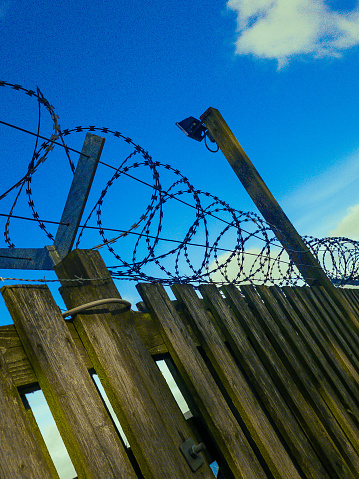 This razorwire is on top of a wooden fence , with a blue sky background. Sending a strong signal of low tech security.