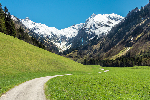 Amazing landscape with snow capped mountains, green grass meadows and winding hiking trail in springtime. Alps, Trettachtal, Allgaeu, Bavaria, Germany.
