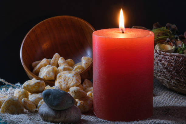 Spa session, aromatic stones, colored candle with fire, dried flowers in a wicker basket on burlap cloth