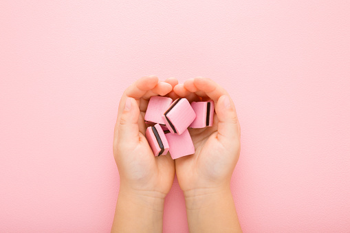 Jelly gummy candies with dark chocolate in baby girl opened palms on light pink table background. Pastel color. Sweet snack. Closeup. Point of view shot. Top down view.