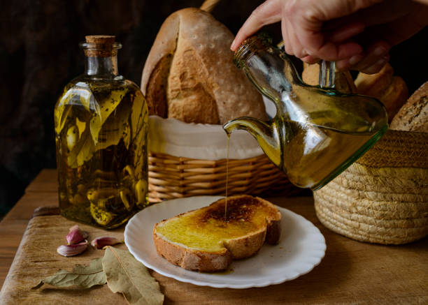 uma mão derramando extra virgin azeite de oliva em uma fatia de pão torrado. - cooking oil extra virgin olive oil olive oil bottle - fotografias e filmes do acervo