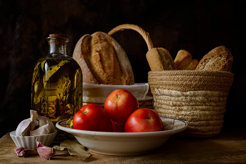 Classic still life with extra virgin olive oil, tomatoes, garlic and bread. Ingredients of a typical breakfast of the Mediterranean diet.