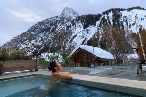 Lady relaxing in hot water SPA pool in nature among snowy mountains