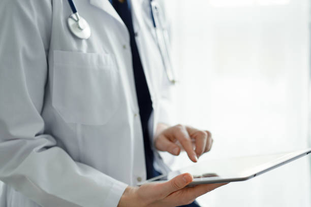 istock Doctor woman using tablet computer while standing near panorama window in clinic, close up. Physician or surgeon at work. Medicine concept 1471640837