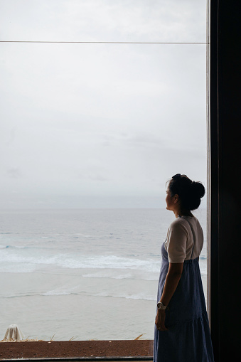 Rear image of young woman looking at the beach from hotel balcony