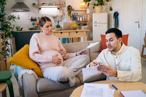 Young Caucasian couple, man and pregnant woman organizing home finances during inflation