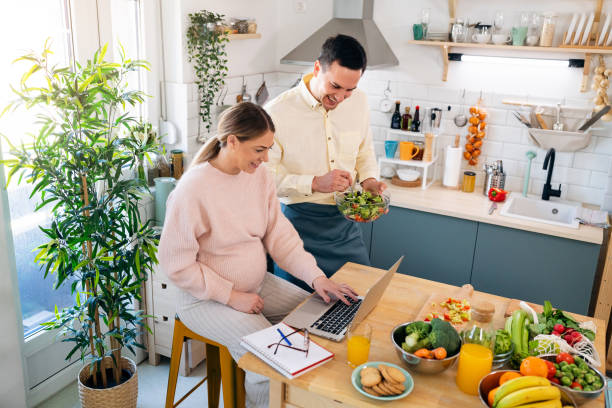istock Man making breakfast while his pregnant girlfriend working on laptop 1471645853