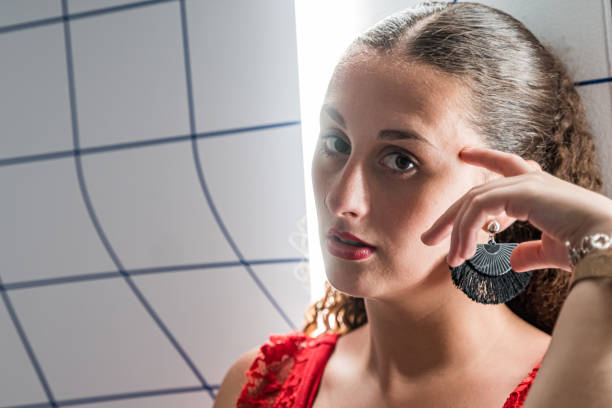 portrait of a young woman with brown curly hair, black earrings, red dress and a backlit spotlight. - earring human face brown hair black hair imagens e fotografias de stock