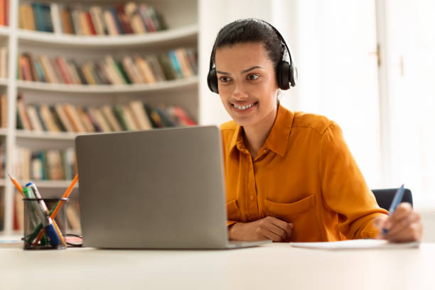 istock Happy female student learning online with laptop, having remote class and taking notes, sitting in library 1471651460