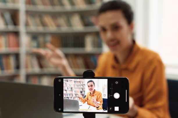 istock Online studying, virtual class. Mixed race female teacher shooting lesson on smartphone camera, sitting in library 1471651462