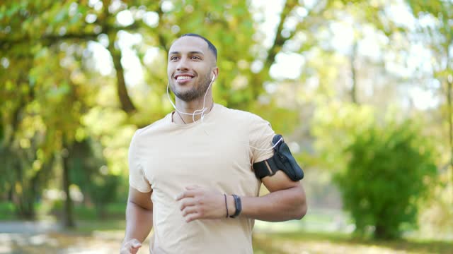 The young runner of mixed race with headphones and a smartphone jogging in an urban city park.