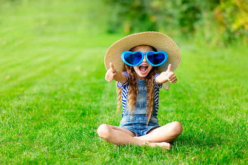 A cute preschool age girl is standing outside at the park and is smiling while looking at the camera.