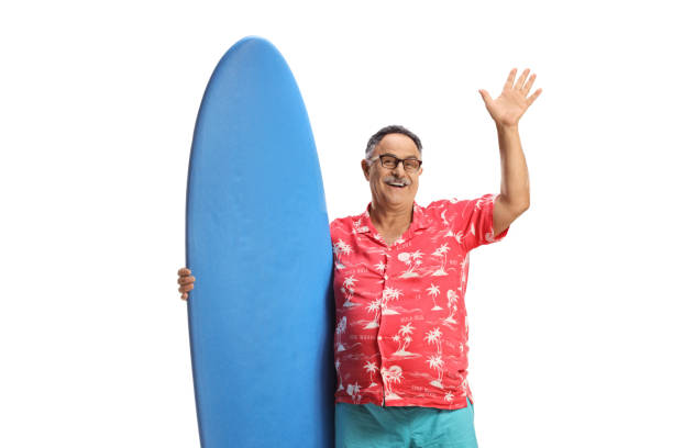 istock Mature man holding a surfing board and waving 1471657145