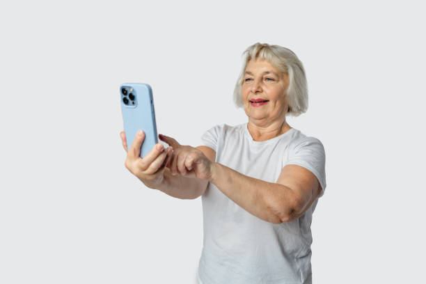 istock Grey senior woman gesturing while taking selfie on mobile phone isolated over white background 1471658020