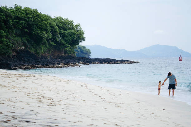 asian man teaching his baby walking on the beach