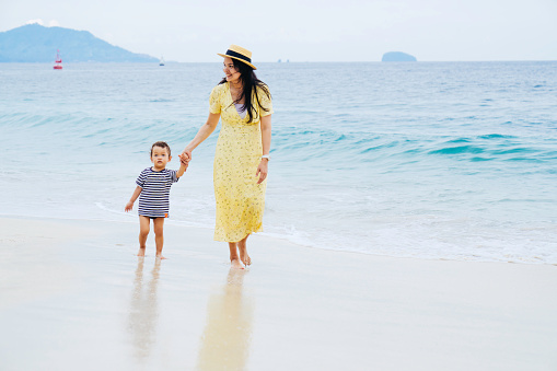 young asian woman teaching her baby walking on the beach
