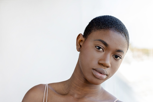 Serious Black woman standing with head tilted to the side, leaning on a window looking at camera. Horizontal portrait close up