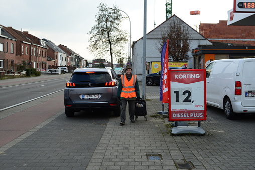 Leuven, Vlaams-Brabant, Belgium - March 6, 2023: retired man wearing a beanie walks with a pick up stick in a hand on the sidewalks in search of other pedestrians' leftover trash on the ground