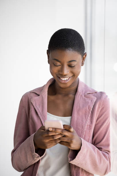 istock Smiling Black woman texting on the smartphone while leaning on glass window 1471662848