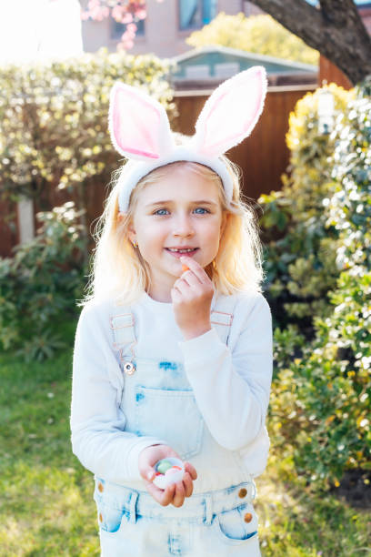 istock Little girl wearing bunny ears holding opened container with Easter chocolate egg sweets and eating candies after traditional egg hunting in garden. Kid having fun on Easter holiday. Selective focus. 1471667386