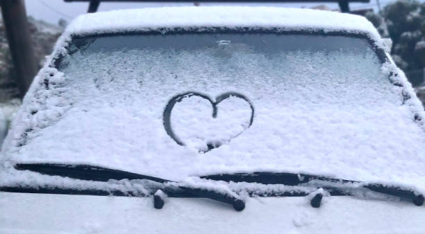 Heart shape drawn by hand on car window covered with fresh snow