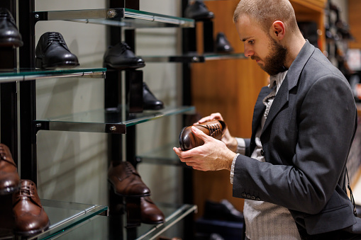 A fashionable young man is walking through the shopping store and choosing shoes to buy.