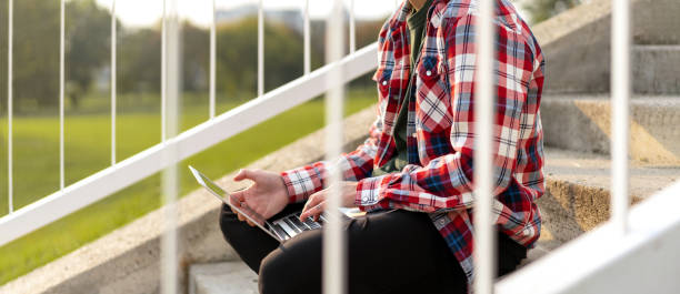 istock Non-binary appearance person sitting on the steps outdoors in park and working on laptop. 1471669849