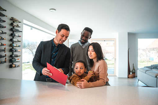 Diverse family buying a new house. Asian male real estate agent giving a diverse family with one child a house tour.