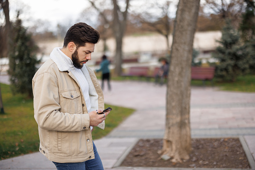 Young man using phone while walking in city park