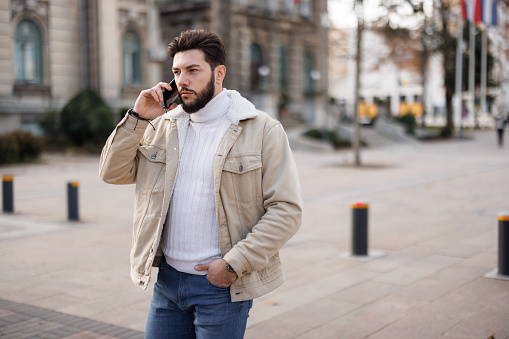Young Caucasian man talking on smartphone while walking in the city