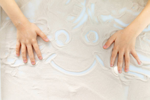 istock hands of a child drawing a smile on the sand 1471673268