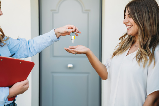 A real estate agent is giving the house keys to her customer. A young woman is receiving the keys.