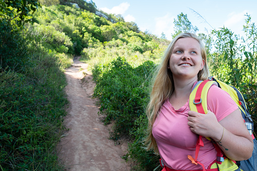 happy female hiker looking at surrounding landscape in forest trail