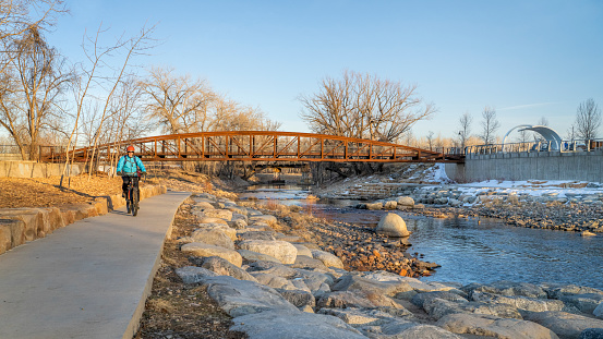 male cyclist is riding a bike in winter sunset scenery - Poudre River Trail in Fort Collins, Colorado at downtown whitewater park, recreation and commuting concept