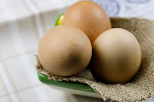 Three boiled hen's eggs are on a piece of linen cloth and have been so placed in a small ceramic bowl