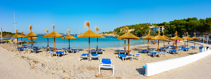 Cala Xinxell cove, Ses Illetes, Majorca, Balearic Islands, Spain. July 20th, 2022 - Panorama of the cove with some apartments in a pinewood and the sand with umbrellas and loungers
