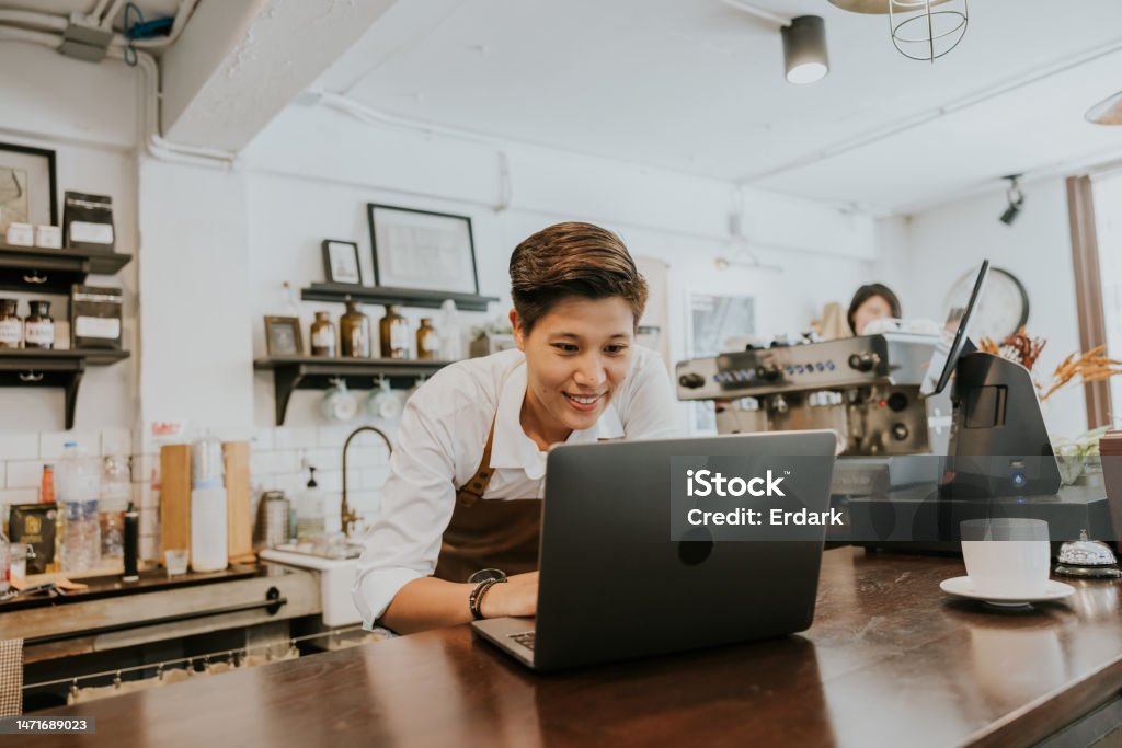 Owner of coffee shop ordering product for her shop from online store. Handsome asian woman using her laptop to ordering some product that using in her coffee shop. Owner Stock Photo
