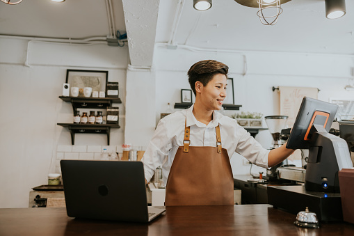 Thai transgender male Owner of coffee shop is working on her cash register and her laptop to checking stock of product and ordering from online store.