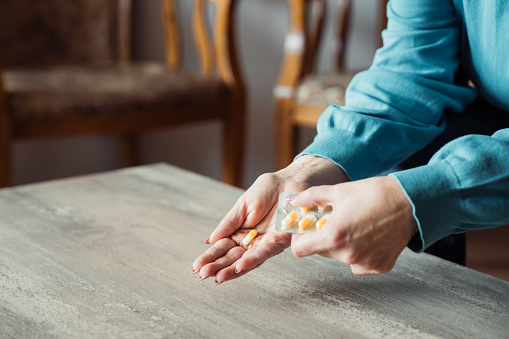 Health conscious person holding a variety of natural vitamins, supplements and herbal remedies, while their other hand holds a glass of water ready to take the pills.