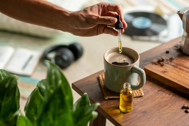 man dropping cbd oil or cannabis oil into a coffee cup while relaxing at home - druppelfles stockfoto's en -beelden