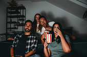 A group of four friends are watching TV at home while they are eating popcorn